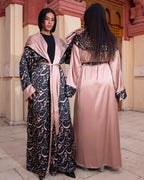 Two women wearing patterned abayas in a decorative setting