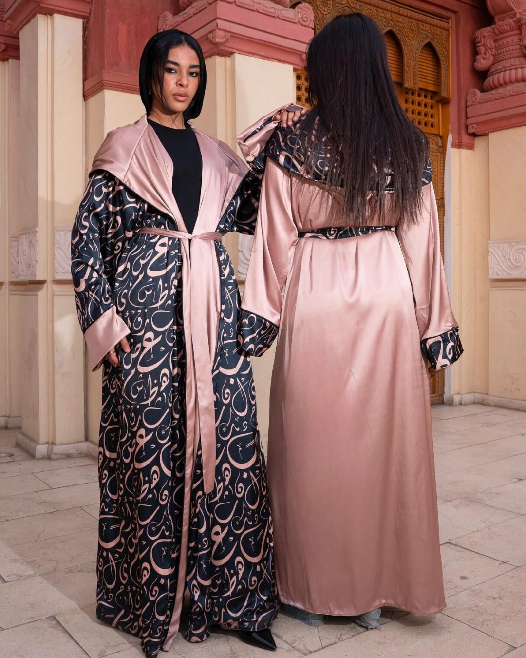 Two women wearing patterned abayas in a decorative setting