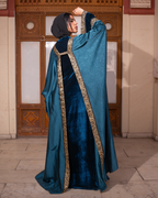 Person wearing a blue abaya with gold embroidery in an indoor setting.